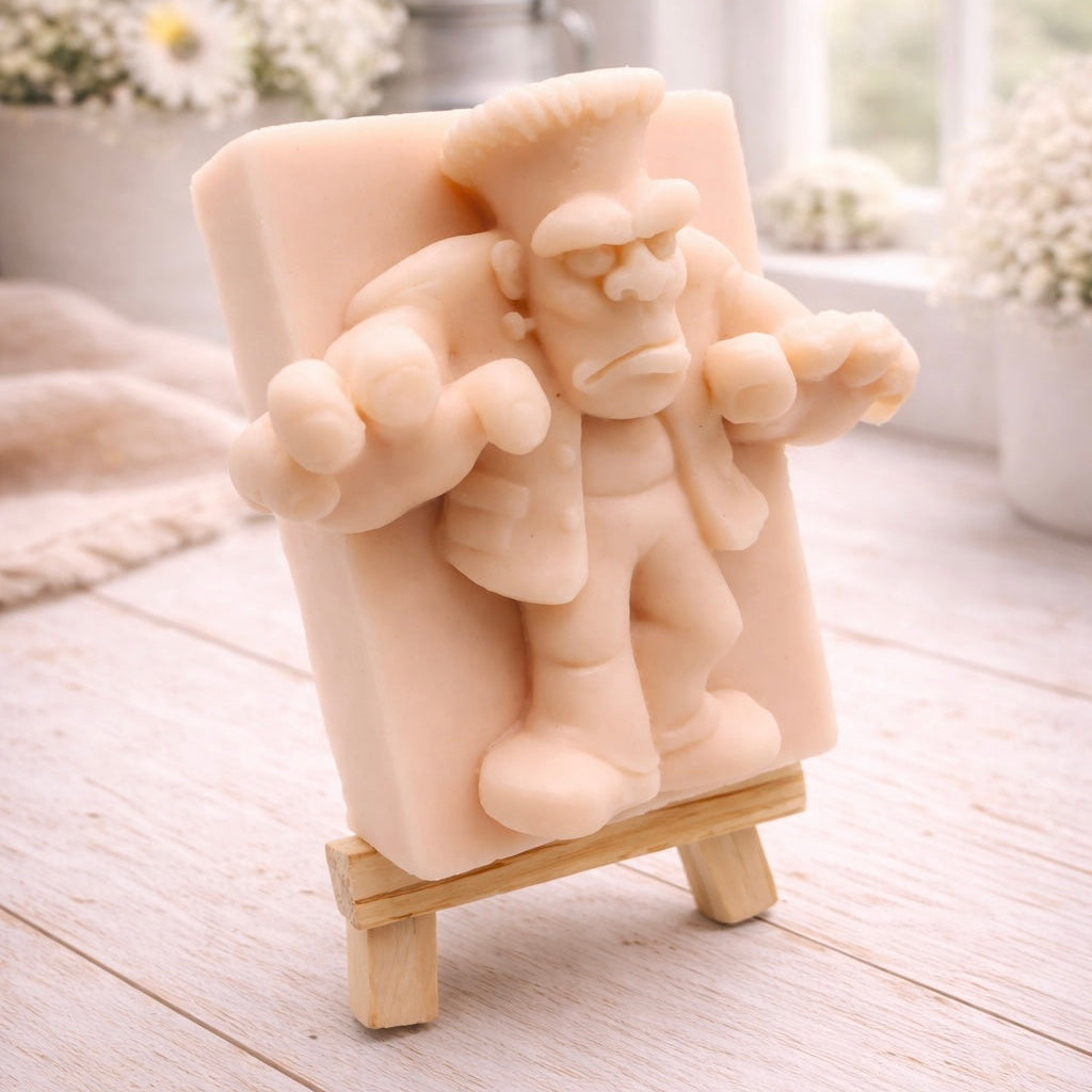 A rectangular handmade vegan soap featuring a high-relief carving of Frankenstein's monster in a classic pose with arms outstretched and a grumpy expression, displayed on a miniature wooden easel.