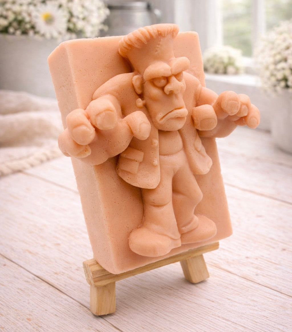 A rectangular handmade vegan soap featuring a high-relief carving of Frankenstein's monster in a classic pose with arms outstretched and a grumpy expression, displayed on a miniature wooden easel.