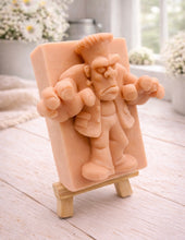Load image into Gallery viewer, A rectangular handmade vegan soap featuring a high-relief carving of Frankenstein's monster in a classic pose with arms outstretched and a grumpy expression, displayed on a miniature wooden easel.
