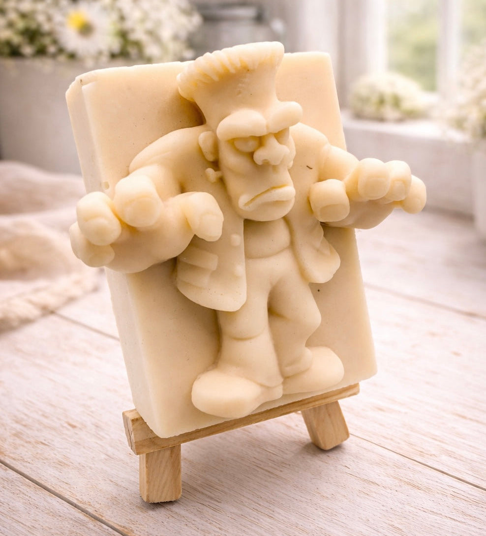 A rectangular handmade vegan soap featuring a high-relief carving of Frankenstein's monster in a classic pose with arms outstretched and a grumpy expression, displayed on a miniature wooden easel.