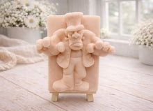 Load image into Gallery viewer, A rectangular handmade vegan soap featuring a high-relief carving of Frankenstein's monster in a classic pose with arms outstretched and a grumpy expression, displayed on a miniature wooden easel.
