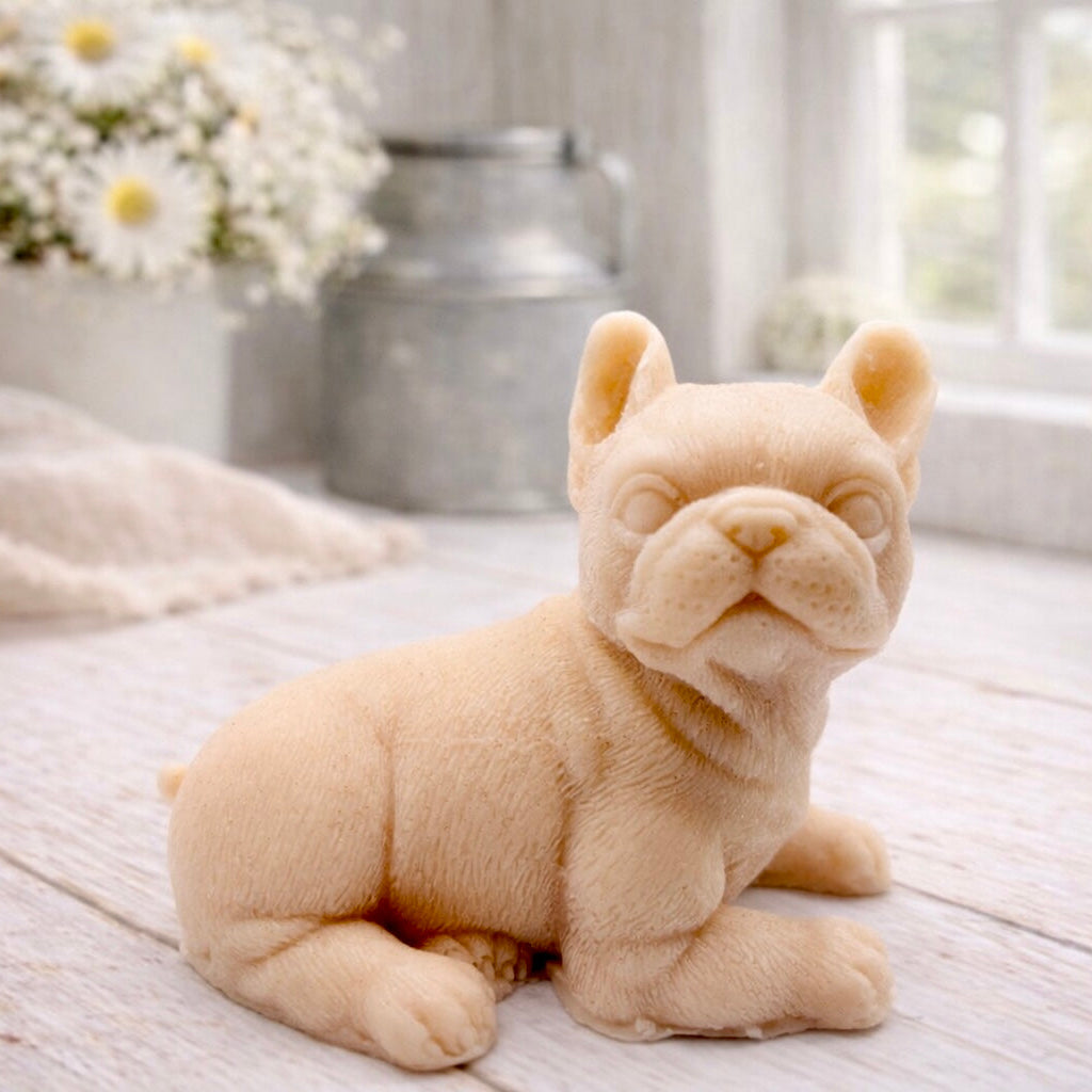 A highly detailed handmade vegan soap in a sophisticated pink tone, sculpted in the shape of a French bulldog puppy sitting upright with its characteristic large ears and wrinkled face, displayed on a light wooden surface.