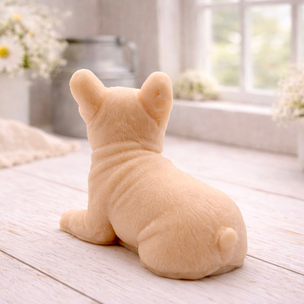 A highly detailed handmade vegan soap in a sophisticated pink tone, sculpted in the shape of a French bulldog puppy sitting upright with its characteristic large ears and wrinkled face, displayed on a light wooden surface.