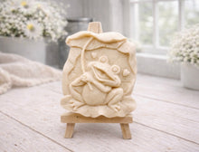 Load image into Gallery viewer, A rectangular handmade vegan soap featuring a high-relief carving of a cheerful, smiling frog sitting on a large lilypad and holding the stem of a leaf over its head like an umbrella.
