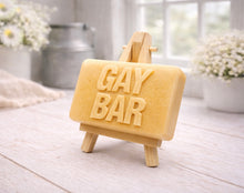 Load image into Gallery viewer, A rectangular handmade vegan soap featuring the words "GAY BAR" in large, bold, 3D block lettering, displayed on a miniature wooden easel.
