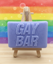Load image into Gallery viewer, A soap bar with 'GAY BAR' text on a wooden stand against a rainbow background
