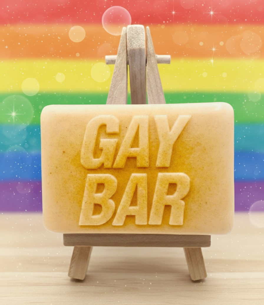 Bar of soap with 'GAY BAR' text on a wooden stand against a rainbow background
