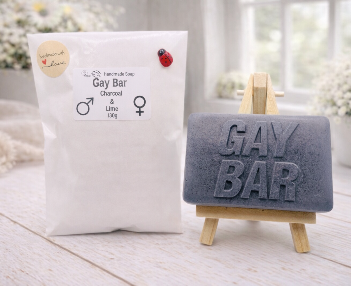 A rectangular handmade vegan soap featuring the words "GAY BAR" in large, bold, 3D block lettering, displayed on a miniature wooden easel.