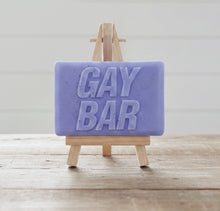 Load image into Gallery viewer, A rectangular handmade vegan soap  featuring the words "GAY BAR" in large, bold, 3D block lettering, displayed on a miniature wooden easel.
