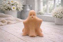 Load image into Gallery viewer, A handmade vegan soap shaped like a friendly ghost with a surprised expression, sitting on a light wood surface with white daisies in the background 
