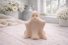 Load image into Gallery viewer, A handmade vegan soap shaped like a friendly ghost with a surprised expression, sitting on a light wood surface with white daisies in the background 
