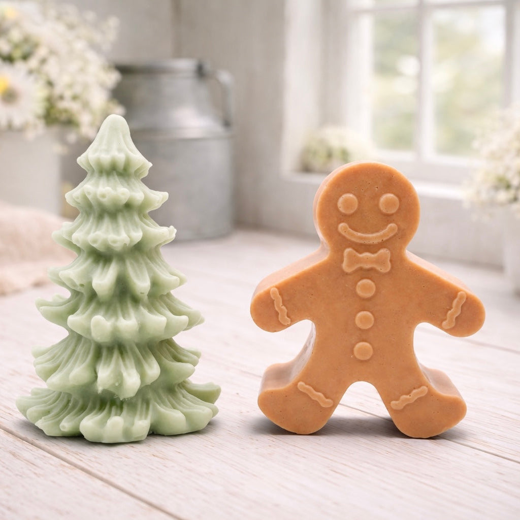A handmade vegan soap featuring a classic gingerbread man with a smiling face, a bow tie, and decorative icing details on his arms and legs, and a Christmas tree - displayed on a miniature wooden easel.