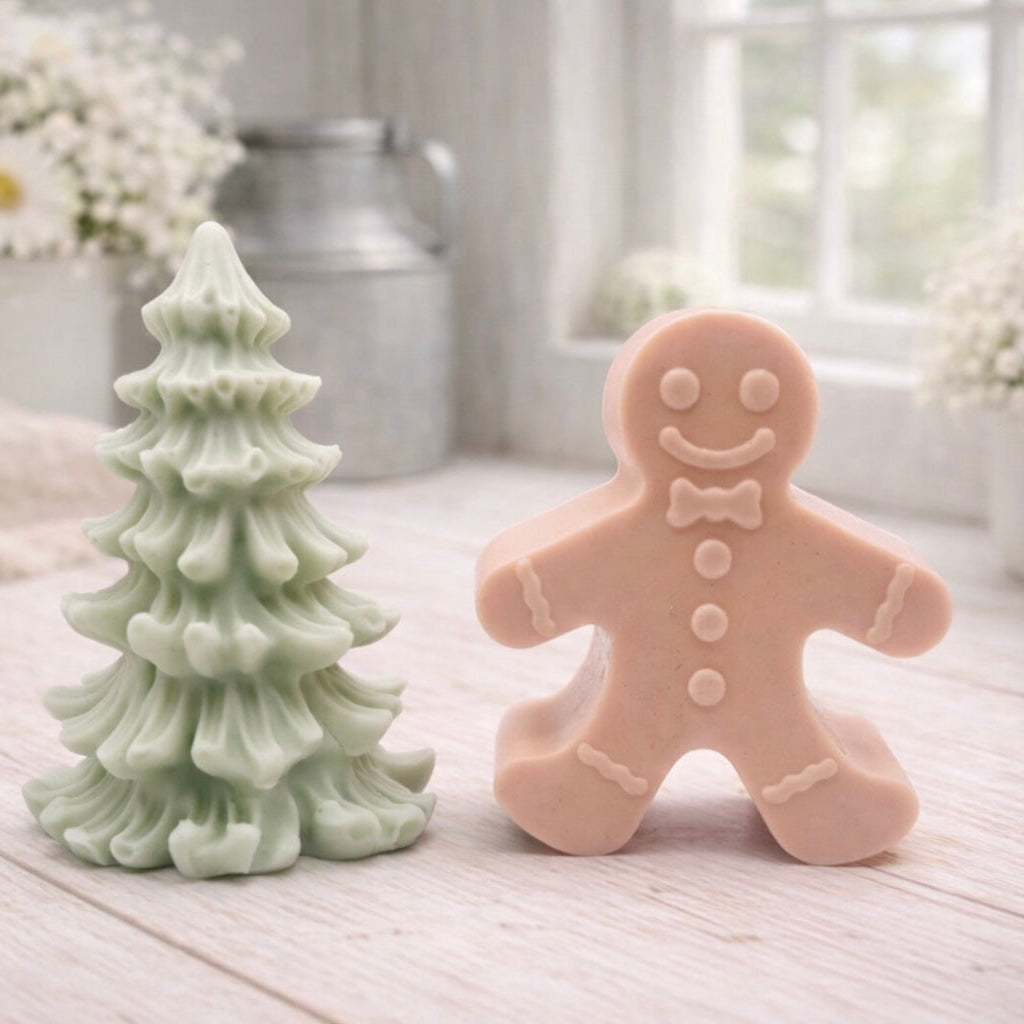 A handmade vegan soap featuring a classic gingerbread man with a smiling face, a bow tie, and decorative icing details on his arms and legs, and a Christmas tree - displayed on a miniature wooden easel.