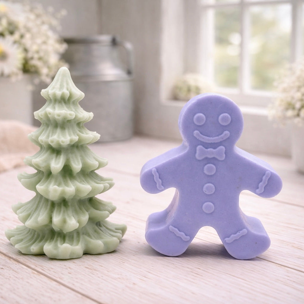 A handmade vegan soap featuring a classic gingerbread man with a smiling face, a bow tie, and decorative icing details on his arms and legs, and a Christmas tree - displayed on a miniature wooden easel.