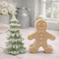 A handmade vegan soap featuring a classic gingerbread man with a smiling face, a bow tie, and decorative icing details on his arms and legs, and a Christmas tree - displayed on a miniature wooden easel.