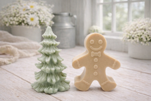 Load image into Gallery viewer, A handmade vegan soap featuring a classic gingerbread man with a smiling face, a bow tie, and decorative icing details on his arms and legs, and a Christmas tree - displayed on a miniature wooden easel.
