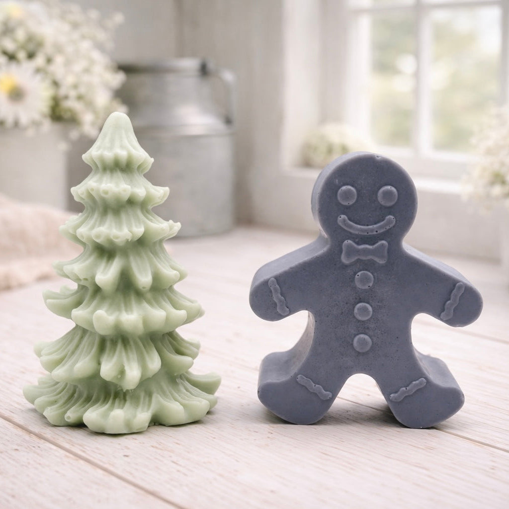 A handmade vegan soap featuring a classic gingerbread man with a smiling face, a bow tie, and decorative icing details on his arms and legs, and a Christmas tree - displayed on a miniature wooden easel.