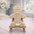 A handmade vegan featuring a classic gingerbread man with a smiling face, a bow tie, and decorative icing details on his arms and legs, displayed on a miniature wooden easel.