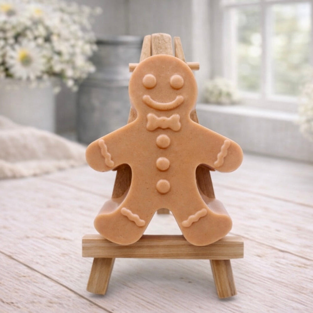 A handmade vegan featuring a classic gingerbread man with a smiling face, a bow tie, and decorative icing details on his arms and legs, displayed on a miniature wooden easel.