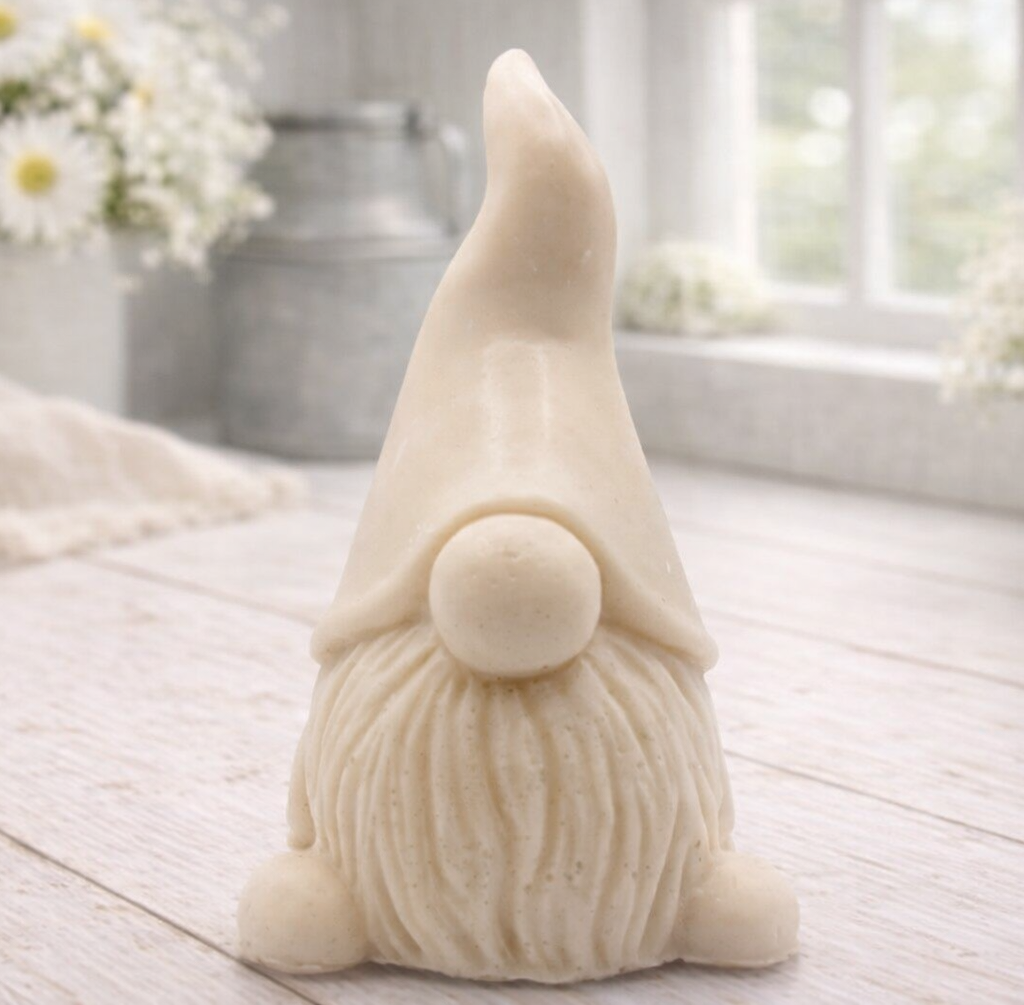 A handmade vegan soap sculpted in the shape of a charming gnome (or gonk), featuring a tall, pointed hat pulled down over the eyes and a full, textured beard, in a natural cream colour.