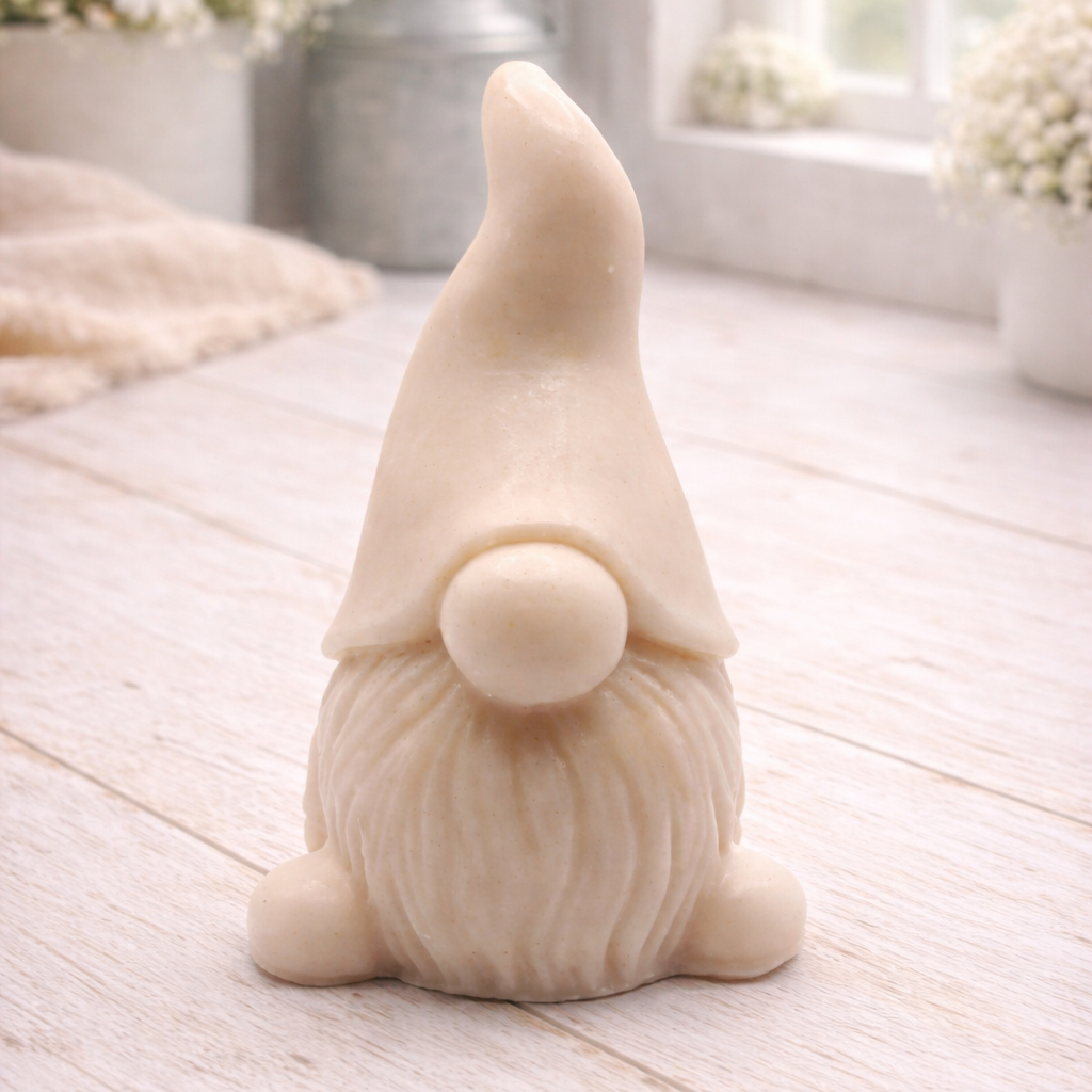 A handmade vegan soap sculpted in the shape of a charming gnome (or gonk), featuring a tall, pointed hat pulled down over the eyes and a full, textured beard, in a natural cream colour.