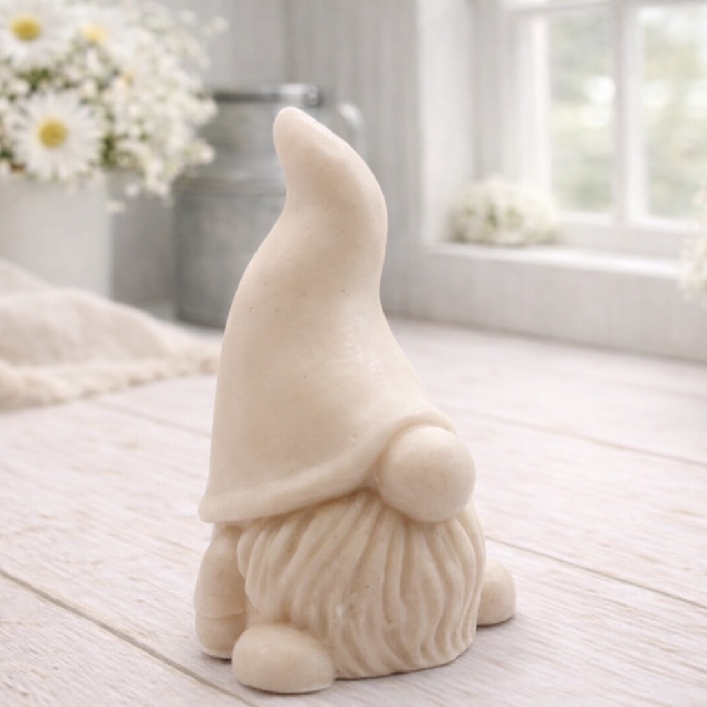 A handmade vegan soap sculpted in the shape of a charming gnome (or gonk), featuring a tall, pointed hat pulled down over the eyes and a full, textured beard, in a natural cream colour.