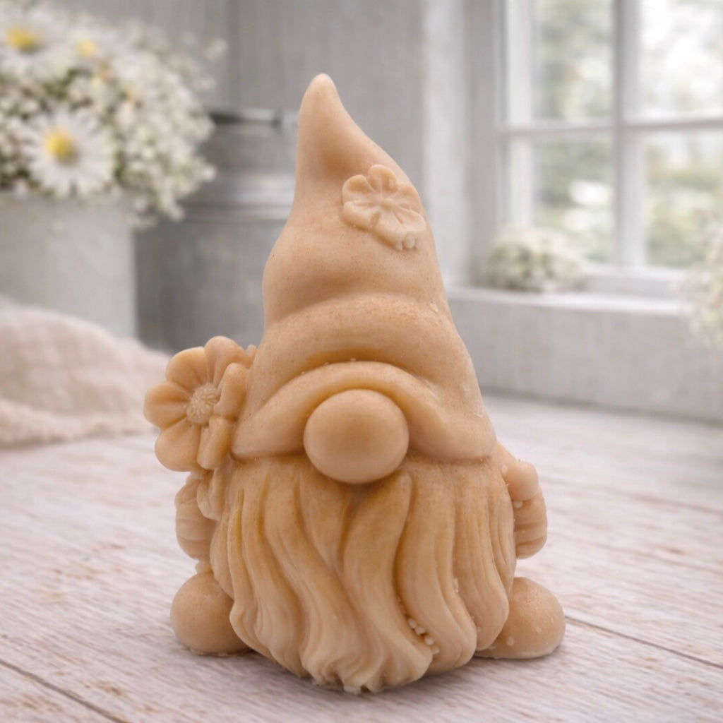 A 3D handmade vegan soap in a warm cream tone, sculpted into a cute garden gnome or gonk with a long flowing beard, a large round nose, and a tall pointed hat adorned with small embossed flowers.