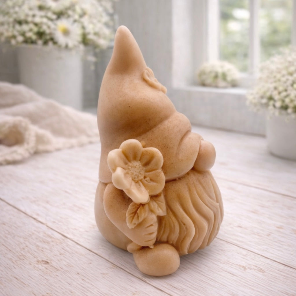 A 3D handmade vegan soap in a warm cream tone, sculpted into a cute garden gnome or gonk with a long flowing beard, a large round nose, and a tall pointed hat adorned with small embossed flowers.