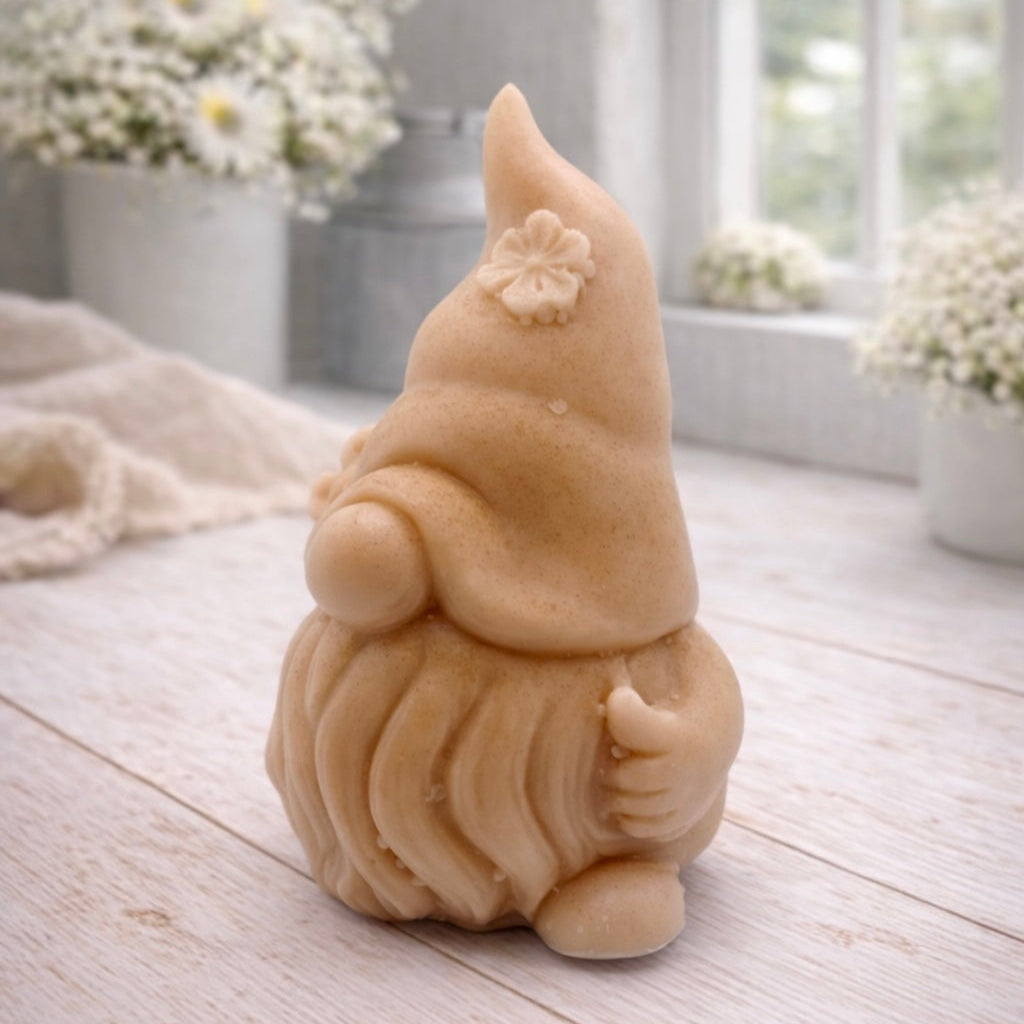 A 3D handmade vegan soap in a warm cream tone, sculpted into a cute garden gnome or gonk with a long flowing beard, a large round nose, and a tall pointed hat adorned with small embossed flowers.