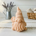A 3D handmade vegan soap in a warm cream tone, sculpted into a cute garden gnome or gonk with a long flowing beard, a large round nose, and a tall pointed hat adorned with small embossed flowers.