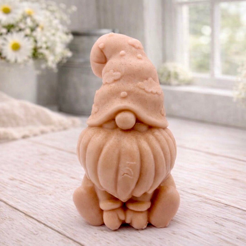 A handmade vegan soap in a natural tone, sculpted as a gnome (gonk) with a tall, curved hat that covers the eyes and has clouds on it, a round nose, and a long, textured beard.