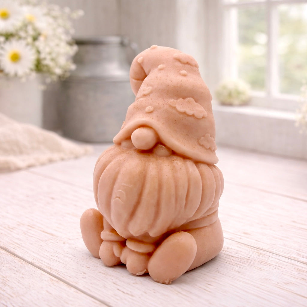 A handmade vegan soap in a natural tone, sculpted as a gnome (gonk) with a tall, curved hat that covers the eyes and has clouds on it, a round nose, and a long, textured beard.