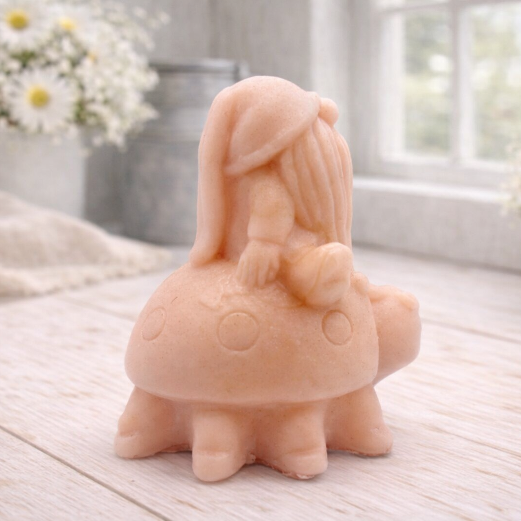 A handmade vegan soap in a warm terracotta-peach tone, sculpted as a whimsical gnome (gonk) with a long, flowing beard sitting on the back of a large, smiling ladybird with visible spots, displayed on a light wooden surface.