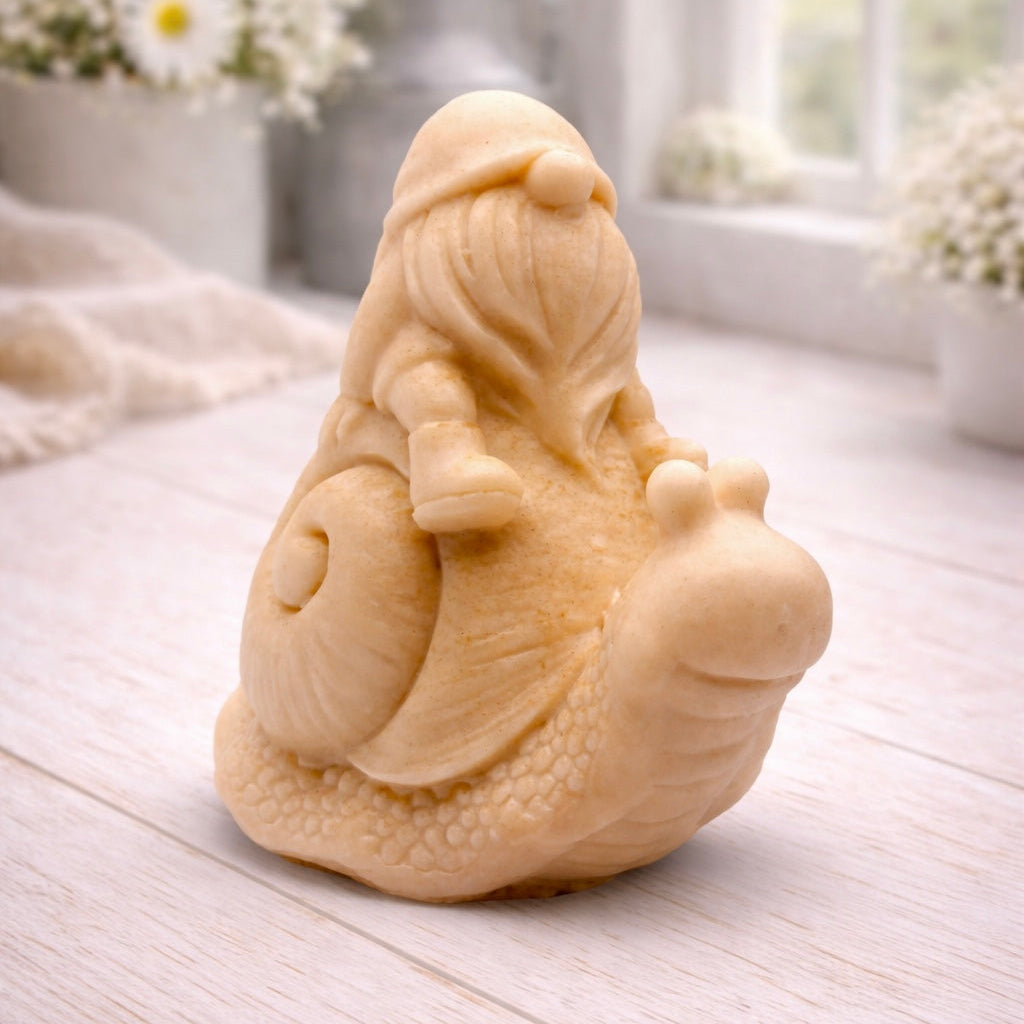 A handmade vegan soap gift, sculpted as a whimsical gnome (gonk) with a tall, slouchy hat and a long beard, sitting on the shell of a large snail with a textured, bumpy body.