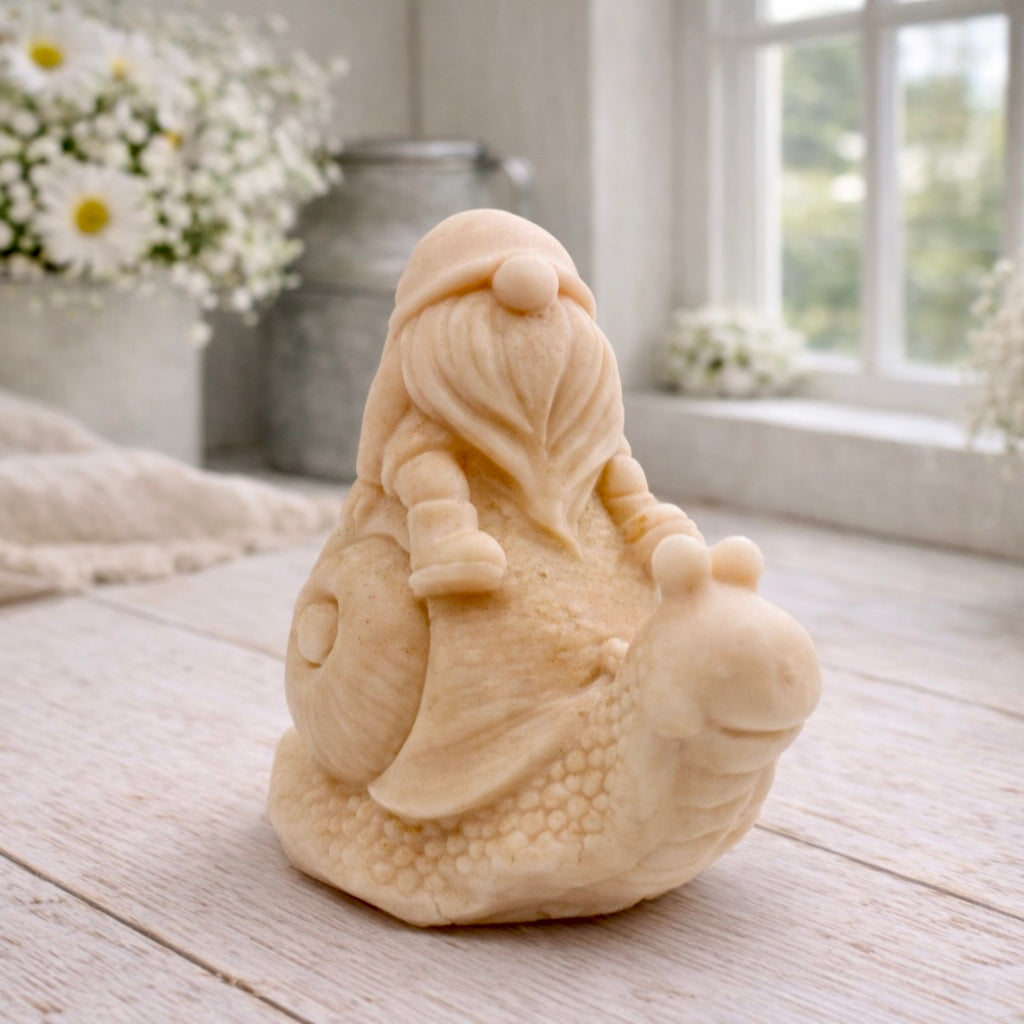 A handmade vegan soap gift, sculpted as a whimsical gnome (gonk) with a tall, slouchy hat and a long beard, sitting on the shell of a large snail with a textured, bumpy body.