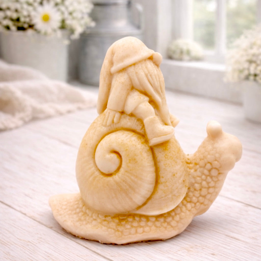 A handmade vegan soap gift, sculpted as a whimsical gnome (gonk) with a tall, slouchy hat and a long beard, sitting on the shell of a large snail with a textured, bumpy body.
