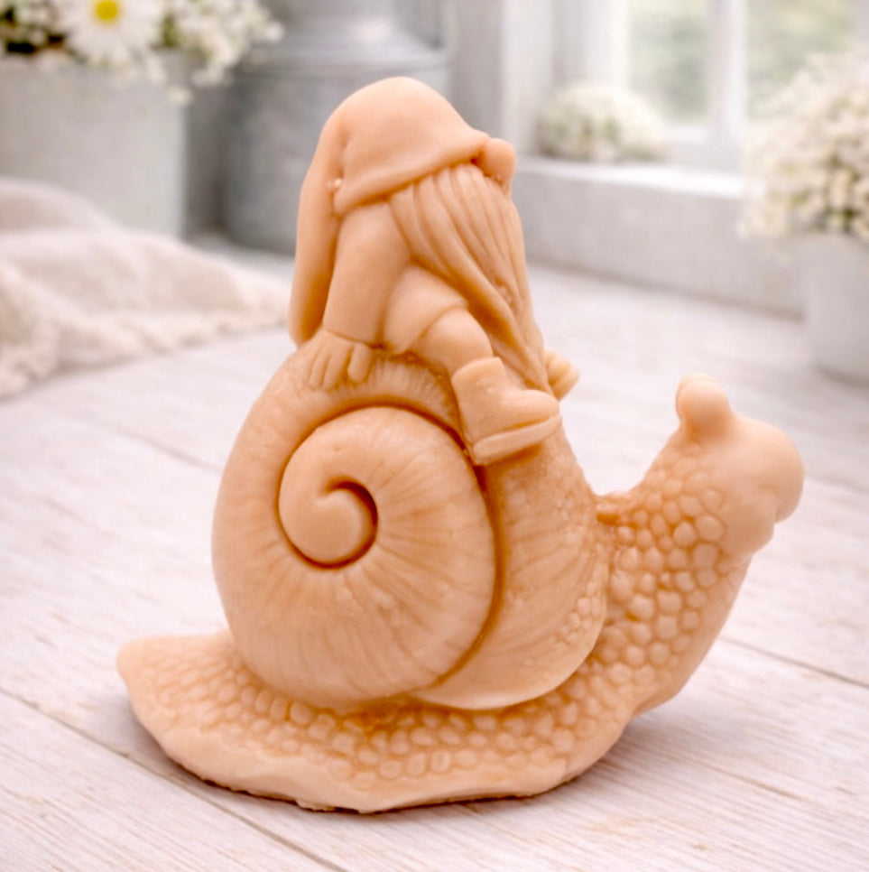 A handmade vegan soap gift, sculpted as a whimsical gnome (gonk) with a tall, slouchy hat and a long beard, sitting on the shell of a large snail with a textured, bumpy body.