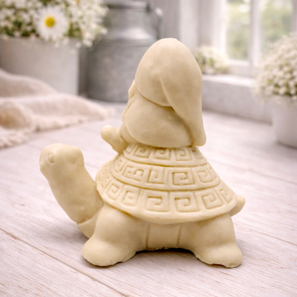 A handmade vegan soap in a natural tone, sculpted as a whimsical gnome (gonk) with a long beard sitting on the back of a large, smiling turtle with a patterned geometric shell.