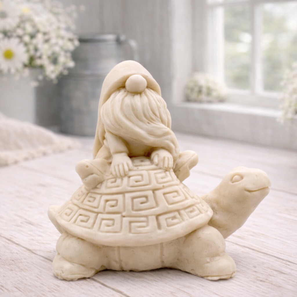 A handmade vegan soap in a natural tone, sculpted as a whimsical gnome (gonk) with a long beard sitting on the back of a large, smiling turtle with a patterned geometric shell.