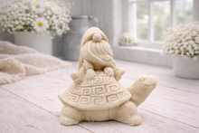 Load image into Gallery viewer, A handmade vegan soap in a natural tone, sculpted as a whimsical gnome (gonk) with a long beard sitting on the back of a large, smiling turtle with a patterned geometric shell.
