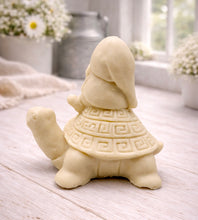 Load image into Gallery viewer, A handmade vegan soap in a natural tone, sculpted as a whimsical gnome (gonk) with a long beard sitting on the back of a large, smiling turtle with a patterned geometric shell.
