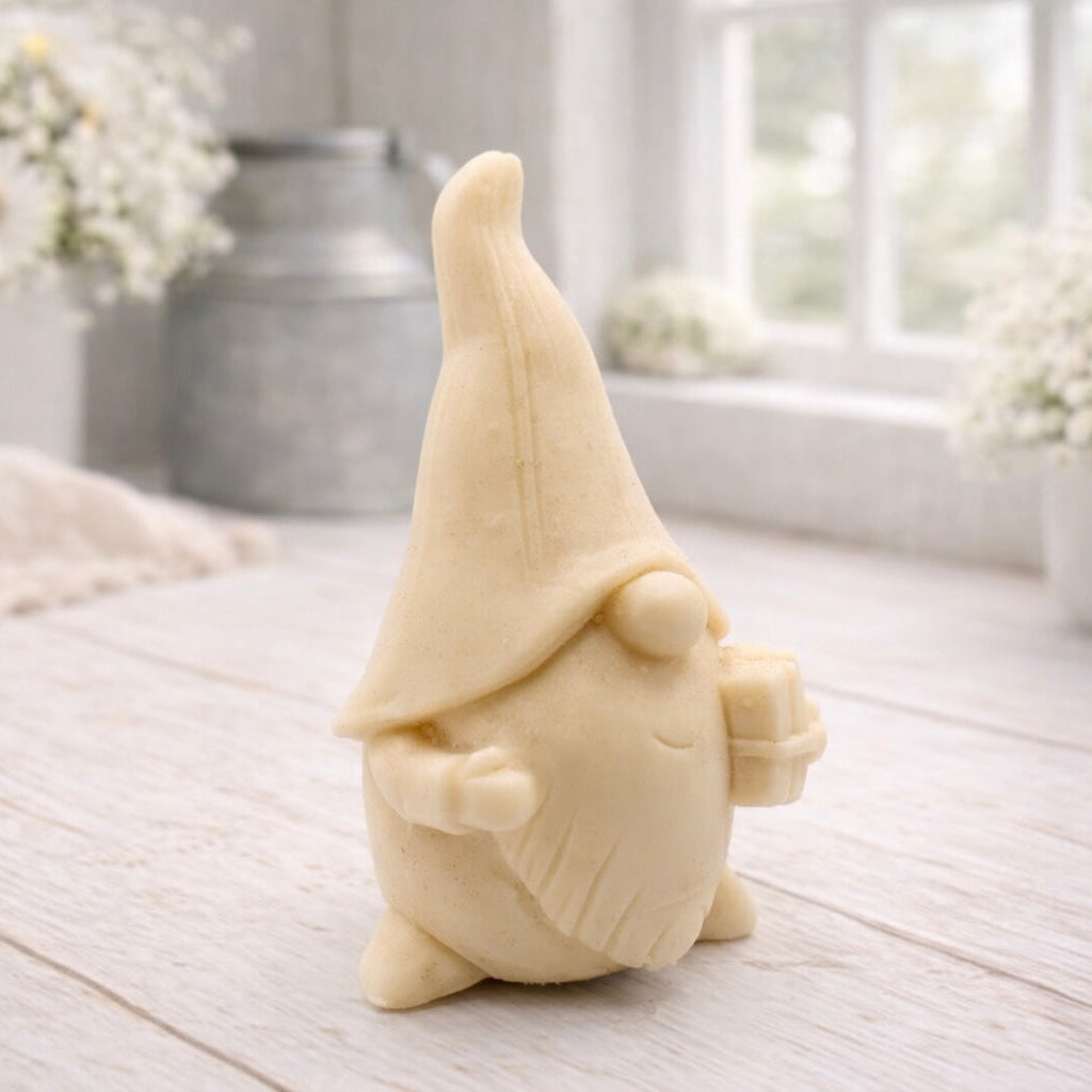 A cream-coloured handmade vegan soap sculpted as a tall, whimsical gnome (gonk) with a pointed hat and long beard, featuring a natural twine hanging rope at the top and displayed in a bright farmhouse setting.