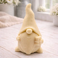 A cream-coloured handmade vegan soap sculpted as a tall, whimsical gnome (gonk) with a pointed hat and long beard, featuring a natural twine hanging rope at the top and displayed in a bright farmhouse setting.