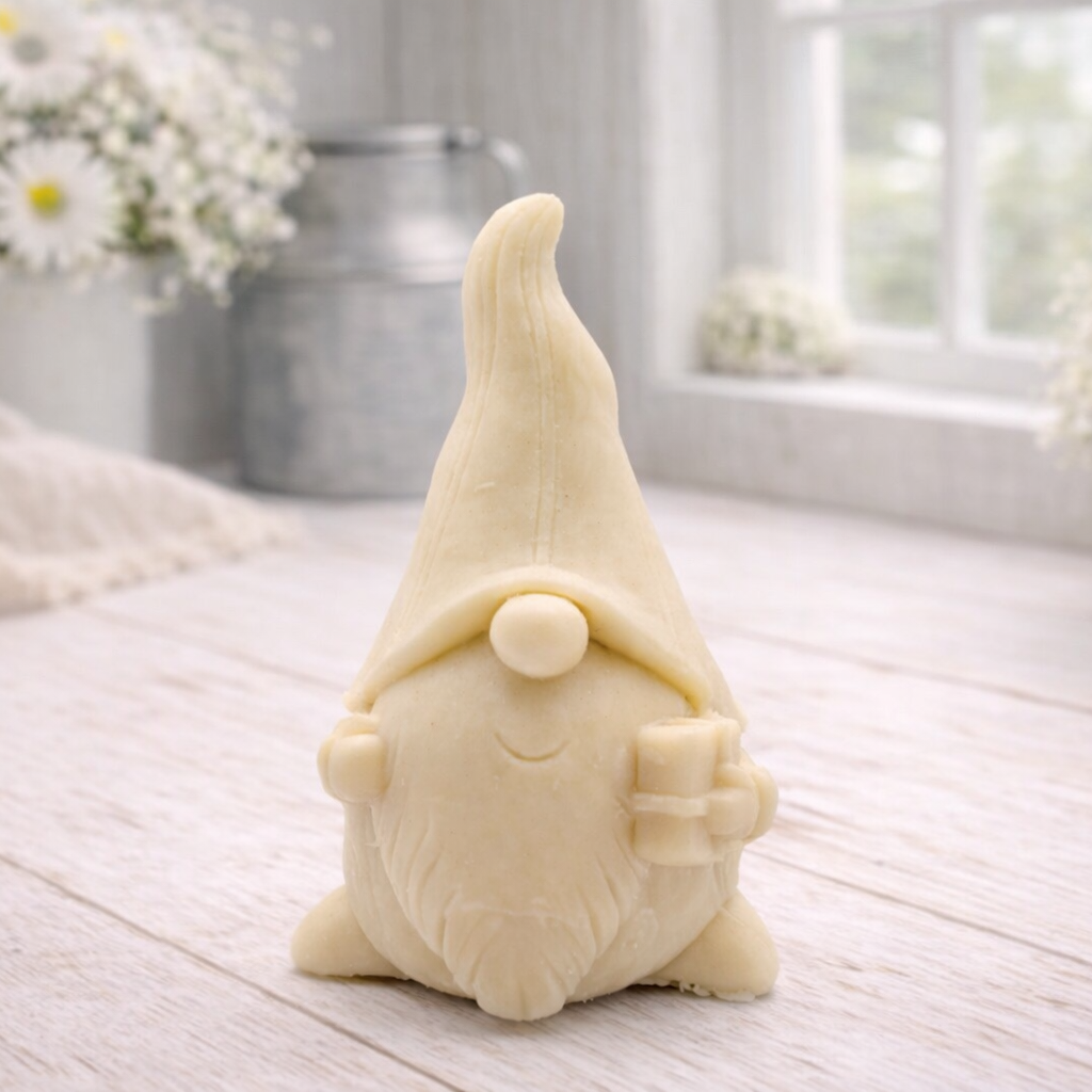 A cream-coloured handmade vegan soap sculpted as a tall, whimsical gnome (gonk) with a pointed hat and long beard, featuring a natural twine hanging rope at the top and displayed in a bright farmhouse setting.