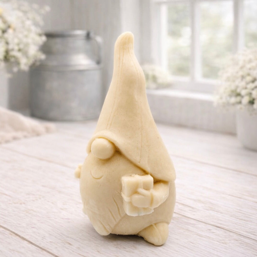 A cream-coloured handmade vegan soap sculpted as a tall, whimsical gnome (gonk) with a pointed hat and long beard, featuring a natural twine hanging rope at the top and displayed in a bright farmhouse setting.