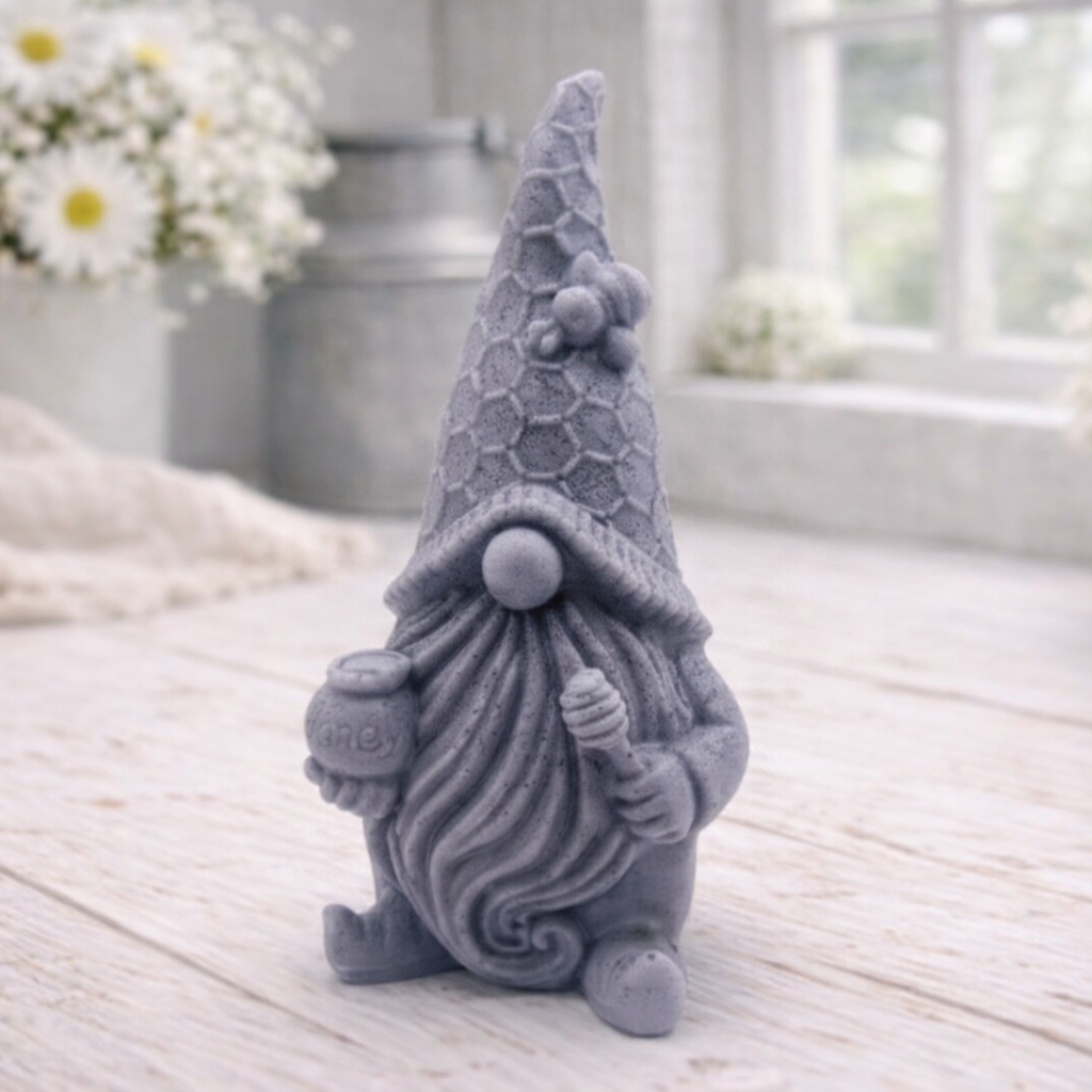 A handmade vegan soap in the shape of a gnome with a long beard, wearing a honeycomb-patterned hat with a bee, holding a honey pot and dipper.