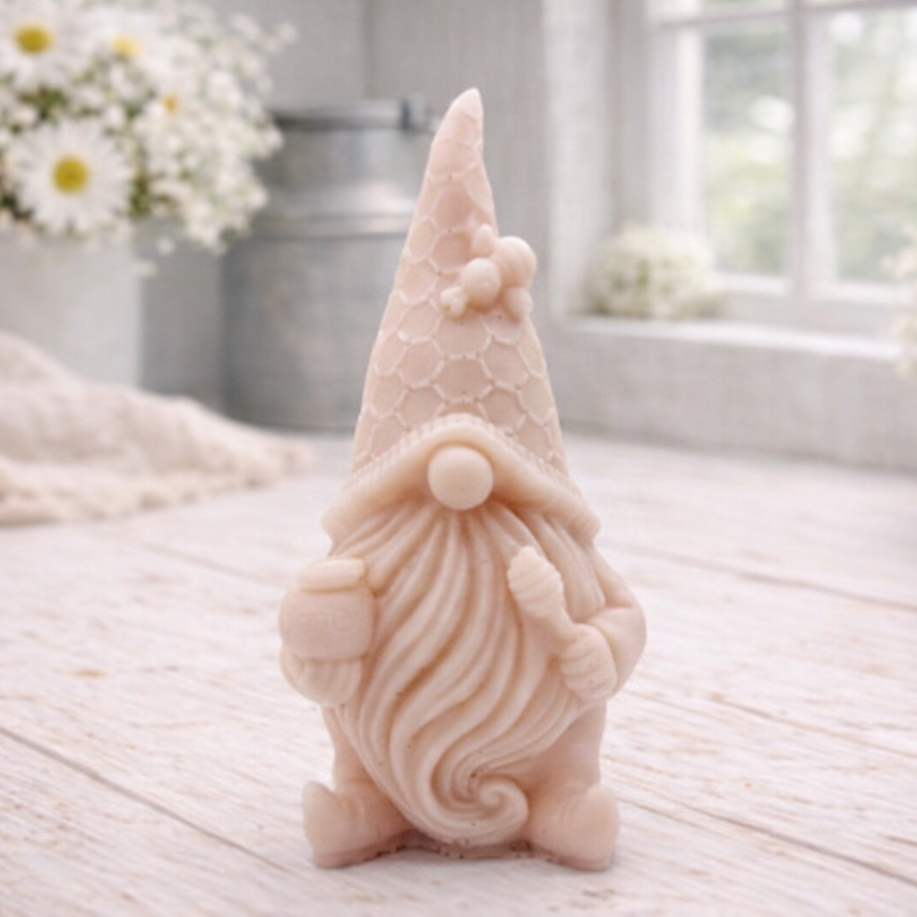 A handmade vegan soap in the shape of a gnome with a long beard, wearing a honeycomb-patterned hat with a bee, holding a honey pot and dipper.