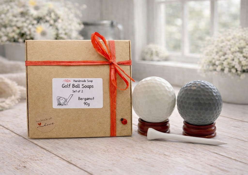 Box of golf ball vegan soaps with two golf balls and a tee on a wooden surface.
