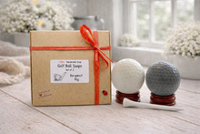 Load image into Gallery viewer, Box of golf ball vegan soaps with two golf balls and a tee on a wooden surface.
