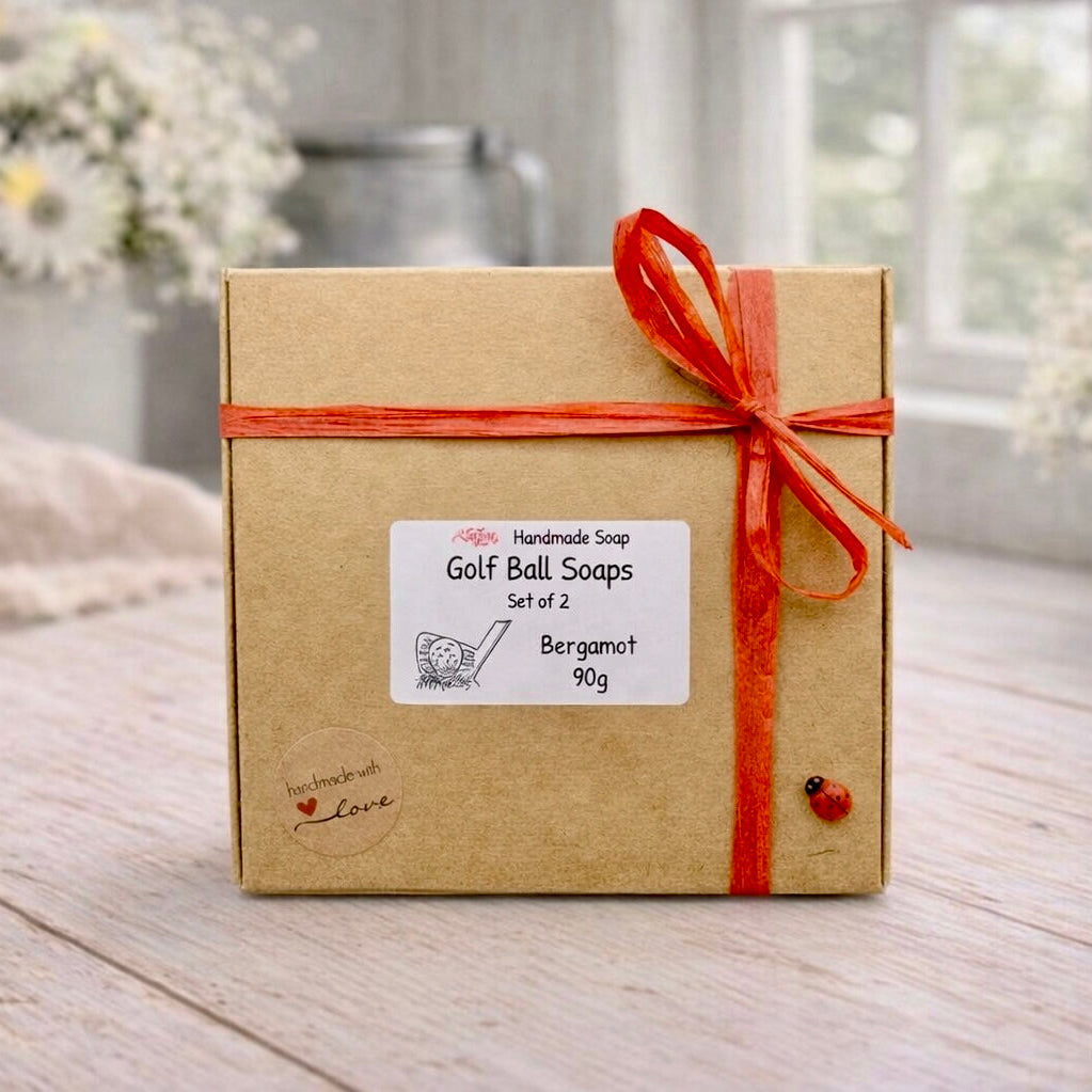 Box of handmade vegan golf ball soaps with a red ribbon on a wooden surface